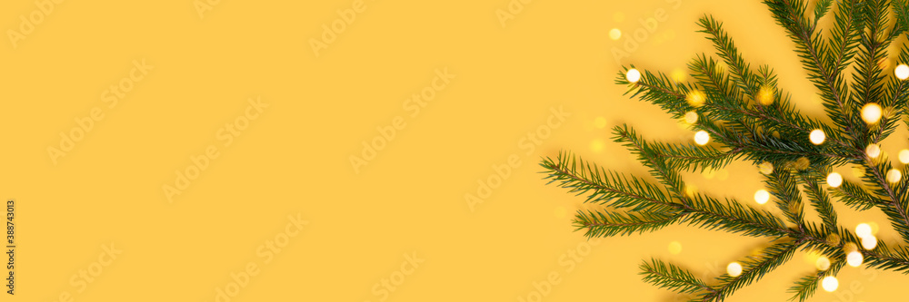 Banner with fir branch and glittering bokeh on a yellow background. Christmas concept with copy space.