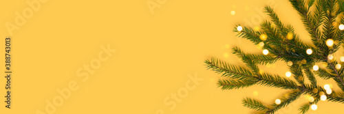 Banner with fir branch and glittering bokeh on a yellow background. Christmas concept with copy space.