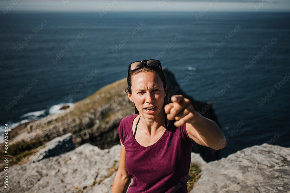 Angry woman looking at camera and pointing with the finger with the coast in the background.