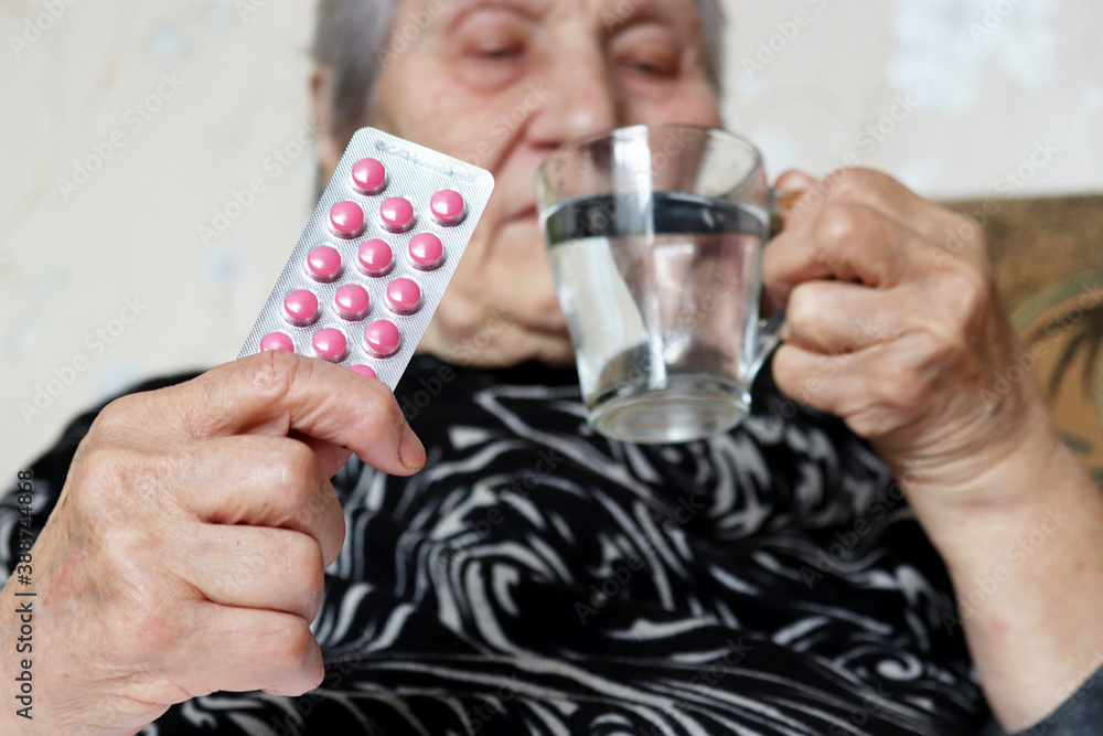 Elderly woman with pills in and glass of water. Concept of medical prescription, sedatives, heart or sleeping pill