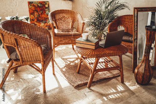 Luxurious and comfortable hotel room in daytime with bamboo chairs and table there are laptop and books with plant on it.