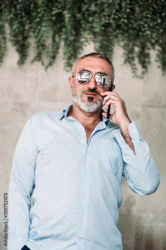 Portrait of middle age man with beard and with sunglasses talking on the phone.