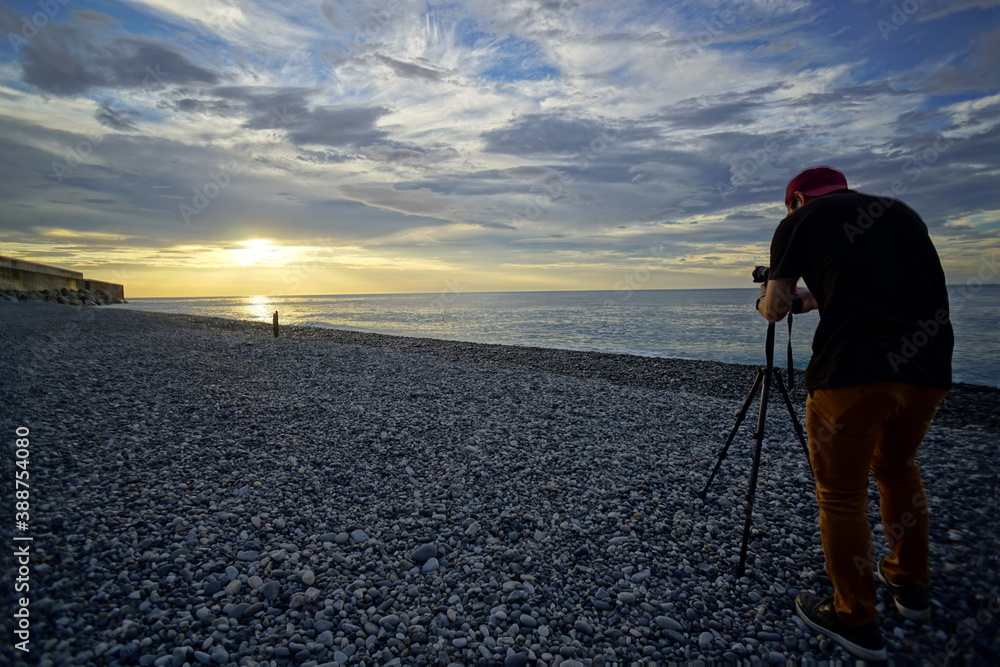 The back view of a man who takes a picture of the sunset over the sea.