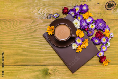 Image of cup of coffee and book with beautiful flowers  on wooden background.