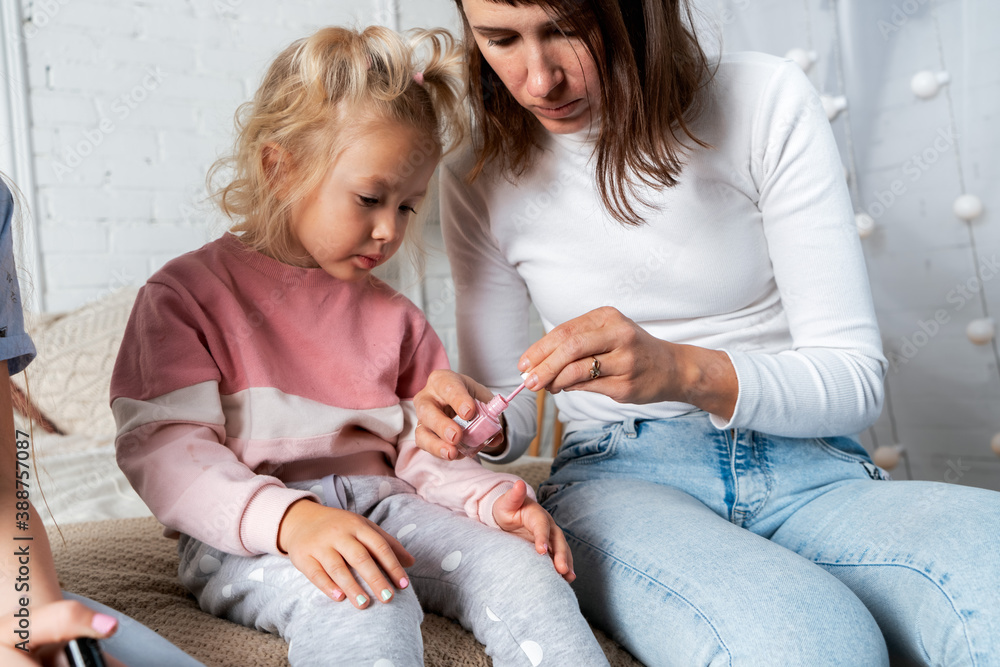 Mom and daughters sit on the bed in the bedroom and paint each other's nails with nail Polish. Mom and daughters sit on the bed in the bedroom and paint each other's nails with nail Polish.