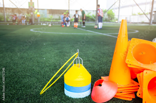 Marker cones and ring and soccer training equipment on green artificial turf with blurry soccer team. Training equipment in academy.