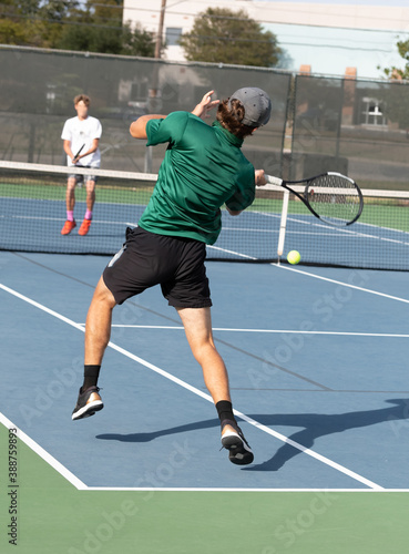 Young boy playing in a competitive tennis match, serving and volleying the ball