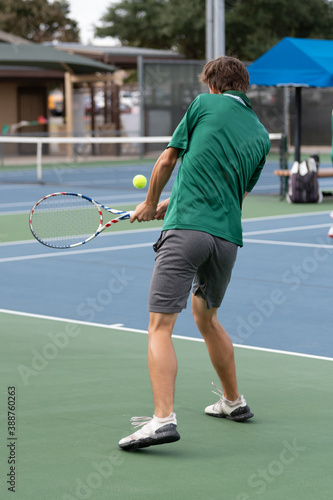 Young boy playing in a competitive tennis match, serving and volleying the ball