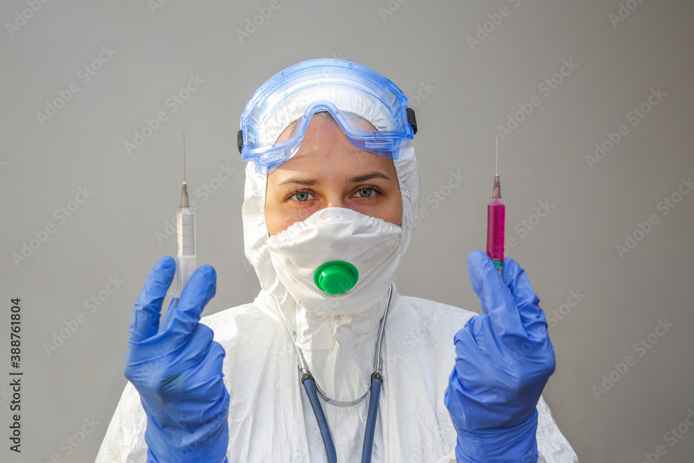 a young female doctor in a protective suit and mask with two syringes a young female doctor in a protective suit and mask with two syringes