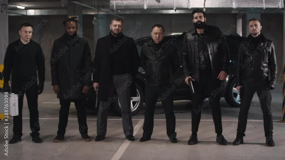 Full portrait of sex multi-ethnic brutal criminals standing in row wearing black clothes holding guns and metal briefcase and black car in background at underground parking Full portrait of sex multi-ethnic brutal criminals standing in row wearing black clothes holding guns and metal briefcase and black car in background at underground parking
