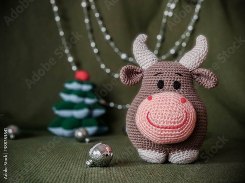 The symbol of the new year 2021. Knitted brown soft toy bull with horns. On green background and silver Christmas decorations.