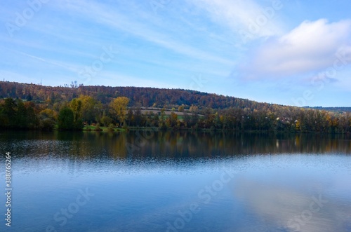 Indian summer at Lake Kratzmuehle in Altmuehltal valley in Bavaria, Germany, blue sky background, colorful fall foliage, reflections on water surface, a sunny day