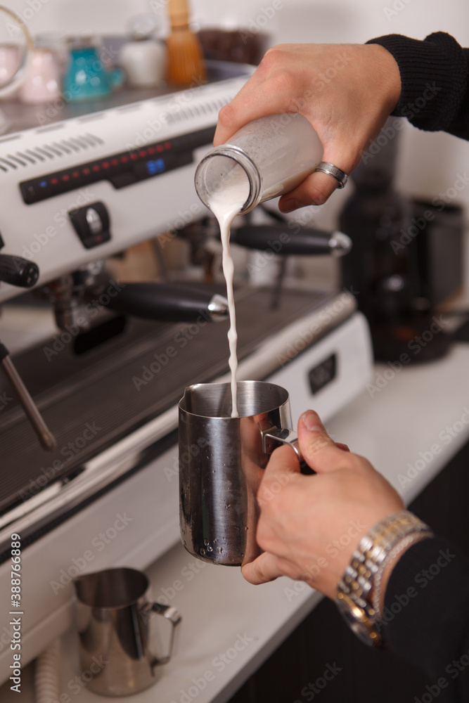 Vertical cropped shot of a male barista pouring milk into frothing pitcher