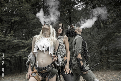 Three girls in torn trash clothes in an apocalyptic manner smoke a hookah.