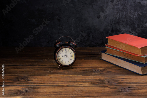 Alarm clock placed on old books on old wooden table black wall background