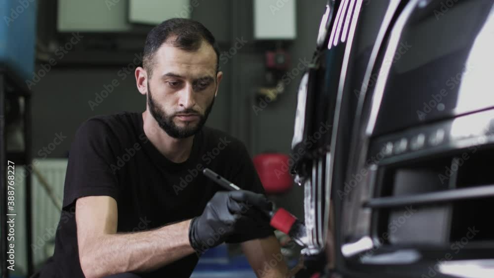 A man in black gloves brushes the front grille of the car. Close-up shot of a car wash worker A man in black gloves brushes the front grille of the car. Close-up shot of a car wash worker