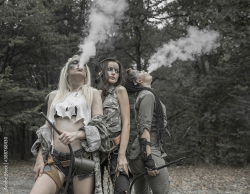 Three girls in torn trash clothes in an apocalyptic manner smoke a hookah.