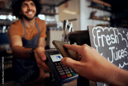 Fotografie Closeup of young female hand making contactless payment in cafe using smartphone