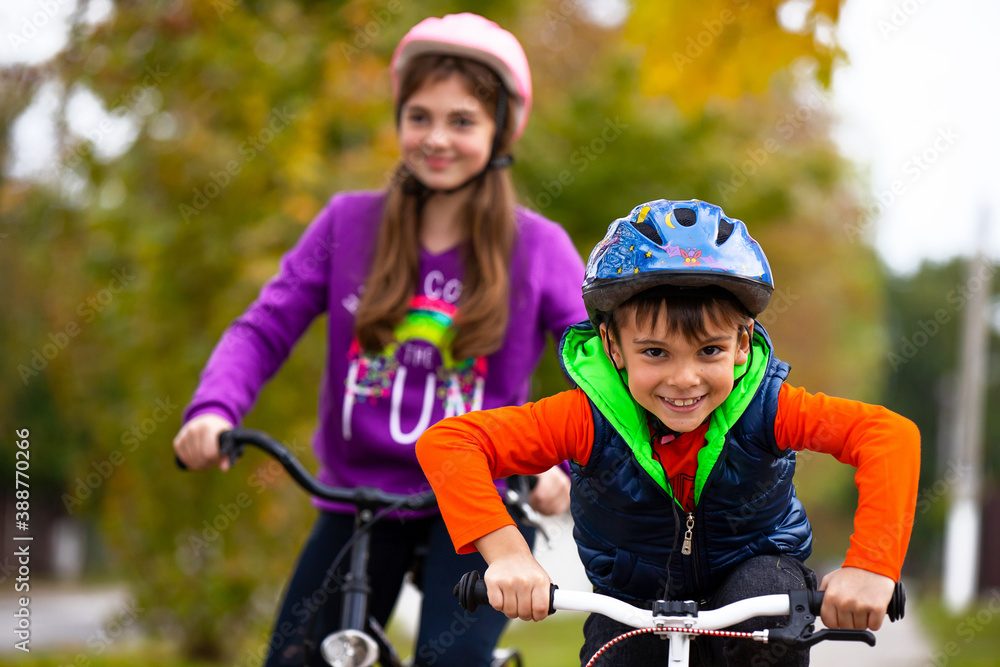 Obraz premium Family holiday. Brother and sister in the park. The boy is alone on the bike. The girl in the background with bicycles on a background of autumn.