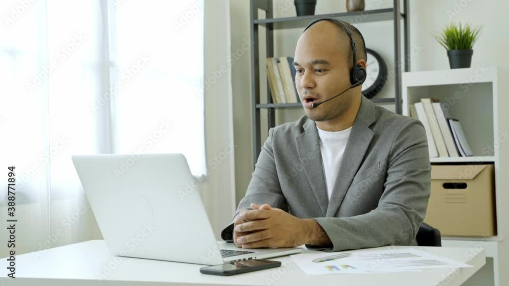 Work from home concept. Asian male business wear a suit and
headphone work at home by video conference sit at home office desk. 4K Resolution. Work from home concept. Asian male business wear a suit and
headphone work at home by video conference sit at home office desk. 4K Resolution.