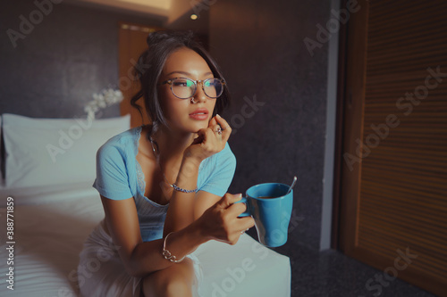Obraz na płótnie Beautiful Asian woman holding and drinking coffee on the bed in the morning in a hotel room w salonie
