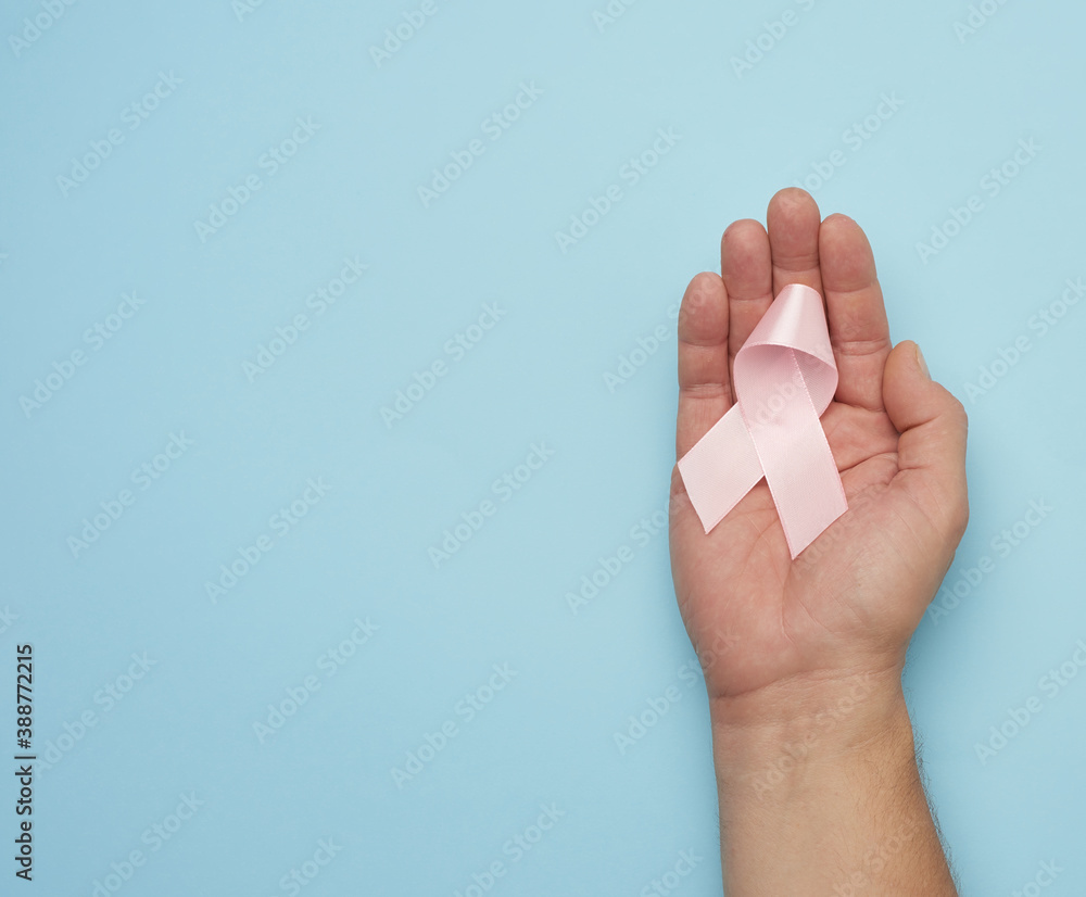 Naklejka premium male hand holds a pink bow-shaped ribbon on a blue background