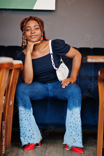 Lovely african american woman with dreadlocks in blue stylish jeans at cafe. Beautiful cool fashionable black young girl indoor.