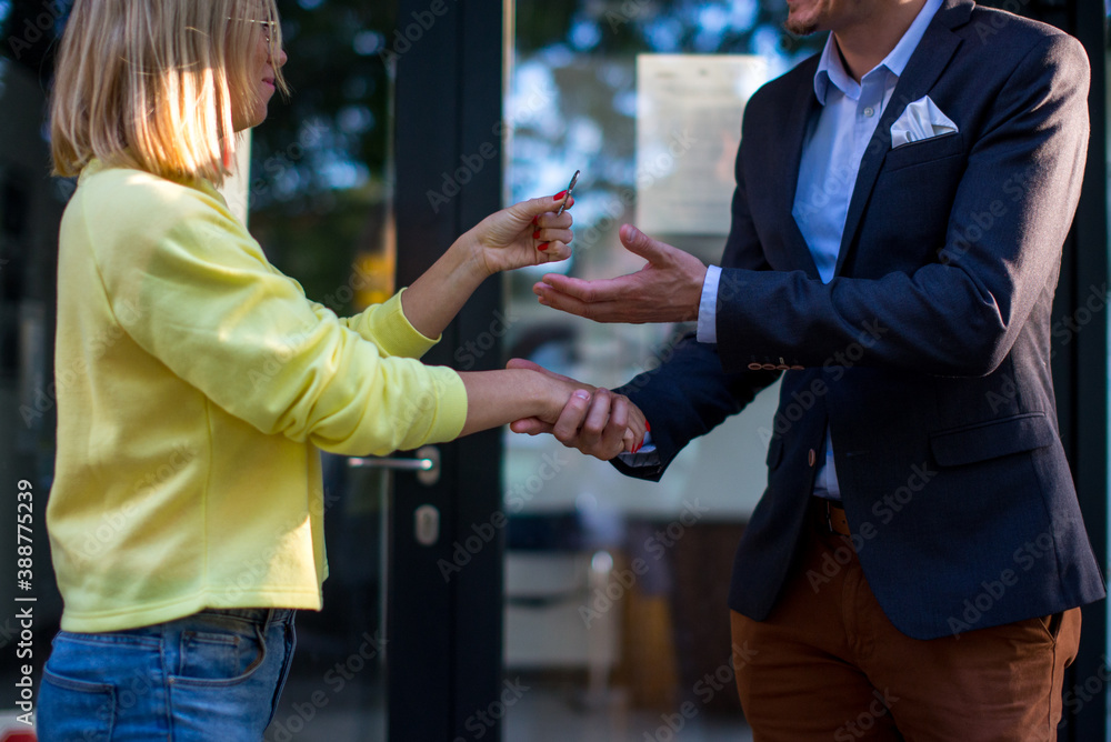The real estate agent gives the man the key to the new apartment. A couple of people are standing in front of a modern building, the woman is holding a key to a new apartment.