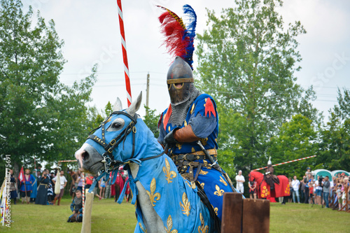 A rider in armor with a spear on a horse. The action takes place at a medieval festival.