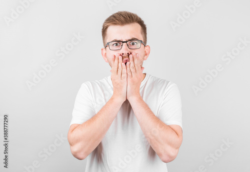 Fototapeta Naklejka Na Ścianę i Meble -  Portrait of a shocked young man covering his mouth with hands