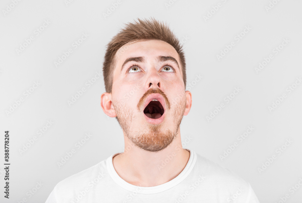 Close up of funny handsome young man with in stylish white t-shirt looking in camera with raised eyebrows and surprised face expression looking up Close up of funny handsome young man with in stylish white t-shirt looking in camera with raised eyebrows and surprised face expression looking up