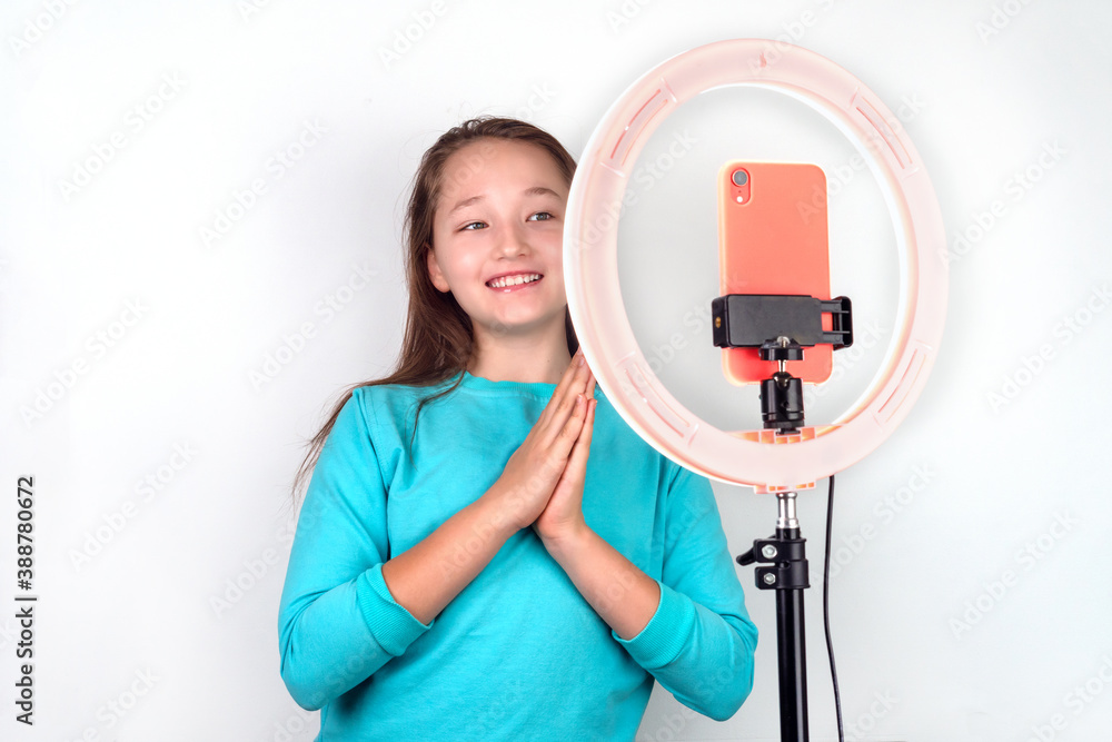 Adorable teenage girl in a blue sweatshirt shoots a selfie video on the phone on a white background. Adorable teenage girl in a blue sweatshirt shoots a selfie video on the phone on a white background.