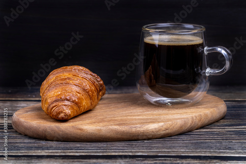 Croissant with a cup of coffee on a wooden board.