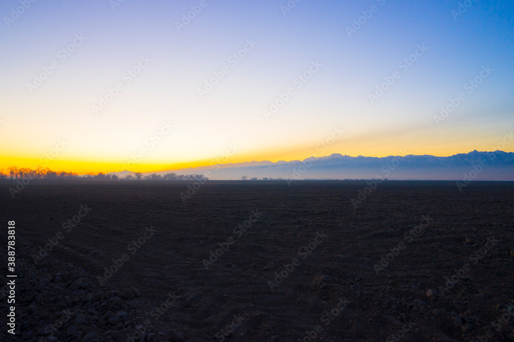 photograph of dawn over a plowed field against a background of mountains.