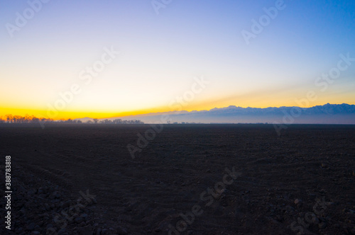 photograph of dawn over a plowed field against a background of mountains.