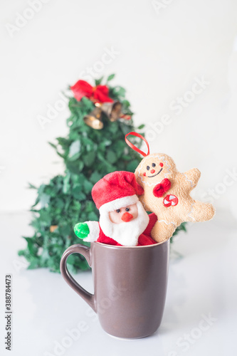 Christmas cookies hugging Santa Claus inside a cup with the Christmas tree behind
