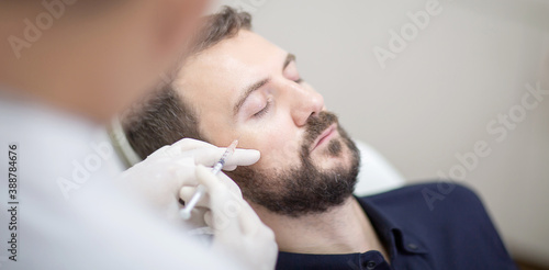 Young man getting beauty facial injections in salon. Beautician makes cosmetic injection into the male patient face crow feet lines. Beauty injections, mesotherapy, revitalization and rejuvenation