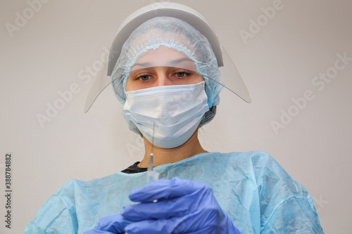 young woman doctor nurse in a protective mask with a syringe in her hand