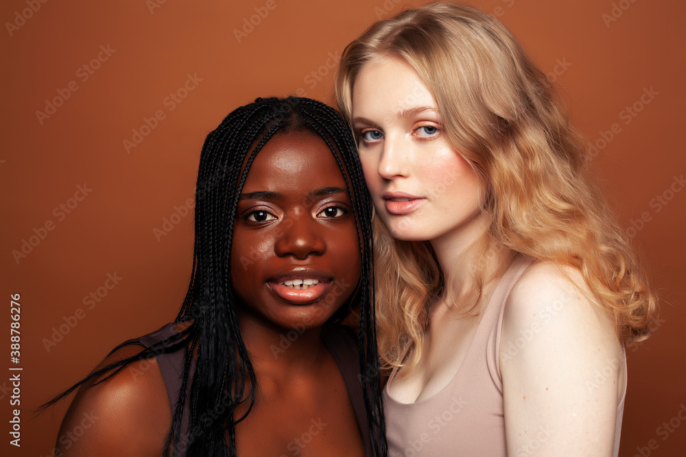 two pretty girls african and caucasian blond posing cheerful together on brown background, ethnicity diverse lifestyle people concept two pretty girls african and caucasian blond posing cheerful together on brown background, ethnicity diverse lifestyle people concept