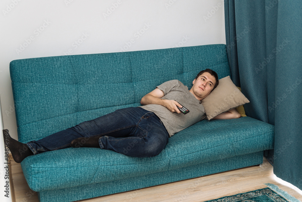 Obraz premium one young man is watching TV lying on the sofa. relax on the weekend, be lazy