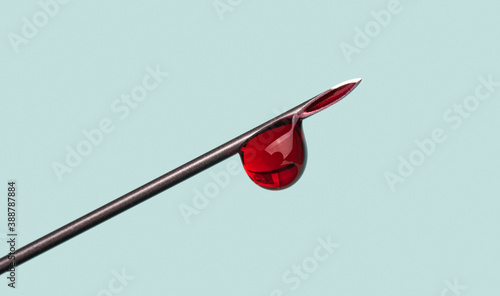 drop of blood on the tip of a syringe needle over blue background