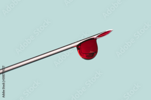 drop of blood on the tip of a syringe needle over light blue background