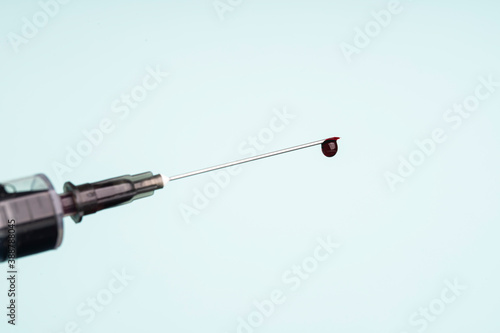drop of blood on the tip of a syringe needle over light blue background