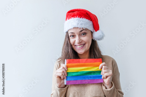 Young woman girl in red Santa Claus hat with LGBT rainbow flag isolated on white background. Happy Christmas and New Year holidays concept.