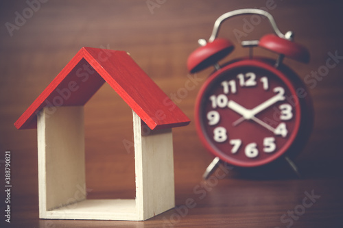 red clock and miniature house on wooden background, copy spaсe.