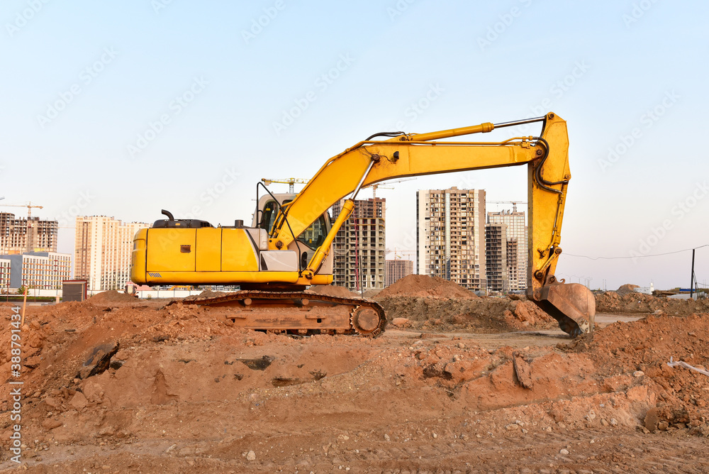 Excavator during excavation and road construction works at construction site on sunset background. Backhoe on foundation work in sand pit. Tower crane on constructing new building