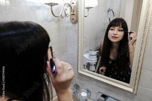 Εκτύπωση καμβά Young woman applying mascara in front of a mirror