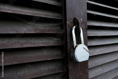 Abandoned locked door of a garage, shed or warehouse. Old and forgotten metal aged padlock on a closed secure facility. Spider web all over. Prison security or isolation during lockdown concept.