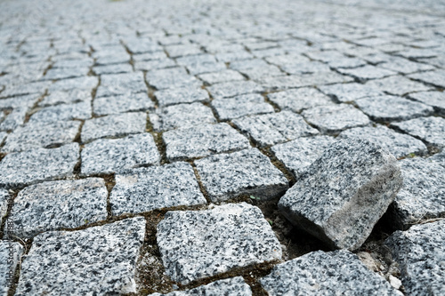 Single cobble out of the structure on a cobblestone street in an old medieval city. Gray paved boulevard made of stones. Urban footpath mosaic from rock material. Outsider in a crowd, special one.