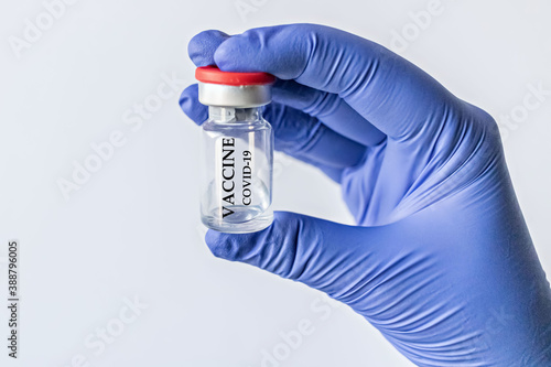 A doctor in a blue medical glove holds a bottle with a coronavirus vaccine. Pandemic concept.